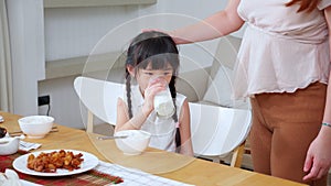 Happiness family with mother and adorable daughter drinking milk or beverage together in the living room.