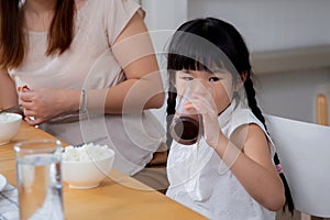 Happiness family with mother and adorable daughter drinking milk or beverage together in the living room.