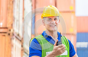 Happiness foreman in hardhat and safety vest talks on two-way radio control loading containers box from cargo