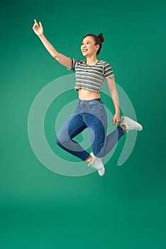 Happiness, freedom, motion and people concept - smiling young woman jumping in air over green background