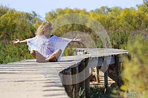 Happiness and freedom. One happy and free woman sitting alone on a wooden pier at the park opening arms and enjoying feeling. photo