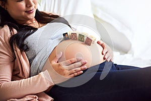 Happiness is on its way. a pregnant woman lying down with wooden baby blocks on her belly at home.