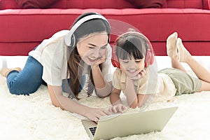 Happiness mother and daughter lie on floor of house use laptop and headphone for entertain