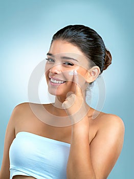 Happiness and tlc is her secret to flawless skin. Studio shot of an attractive young woman applying moisturiser on her