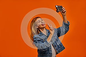 Happiness woman in a jeans jacket shows a peace symbol and take a photo on the camera