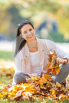 Happiness woman sitting in autumn park holding bouquet with fall leaves