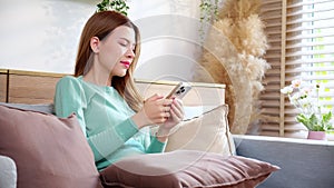 Happiness young asian woman smile sitting on sofa using smart phone with cozy in living room at home.