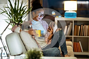 Happiness young entrepreneur woman using her smart phone while drinking a cup of coffee sitting on couch in the office