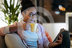 Happiness young entrepreneur woman using her smart phone while drinking a cup of coffee sitting on couch in the office