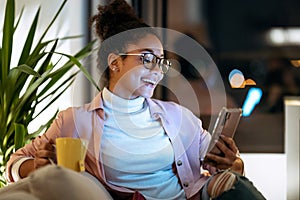 Happiness young entrepreneur woman using her smart phone while drinking a cup of coffee sitting on couch in the office