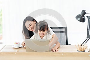 Happiness young mother and daughter sit on a chair in the house, look at laptop for entertain and education, smile and laughing