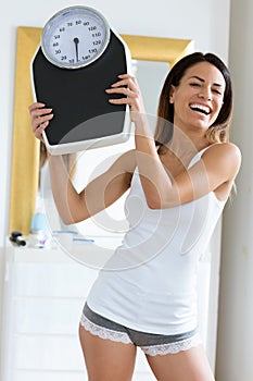 Happiness young woman holding weigh scale while looking at camera at home