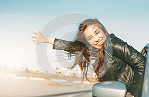 Happpy beautiful charming brunette long hair young asian woman in black leather jacket in car window at sunset