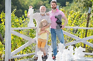 Happt grandfather father and son playing chess. Men in different ages playing chess board game. Three men generation.