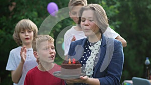 Happy 12 years old teenage girl celebrating birthday with friends blowing out candle on cake in slow motion. Cheerful