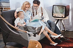 happy 1950s style family sitting on sofa and reading