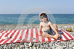 Happy 2 years boy in sunglasses sits on stone beach