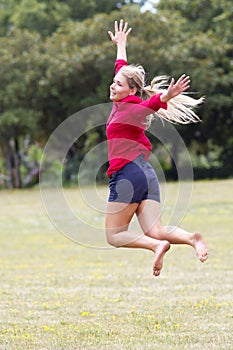 Happy 20s woman jumping high with happiness in sunny park