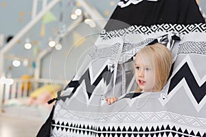 Happy 3 years old blonde girl watching out of playhouse tent in playroom
