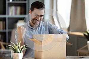 Happy 30s young man celebrating getting purchase from internet store.