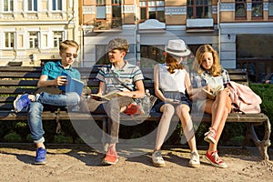 Happy 4 teenage friends or high school students are having fun, talking, reading phone, book. Friendship and people concept, city