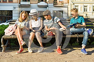 Happy 4 teenage friends or high school students reading books sitting on a bench in the city.