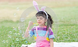 Happy 4 year old Caucasian little girl with bunny ears blowing soap bubbles in park, having fun, sunny day. Cute child playing
