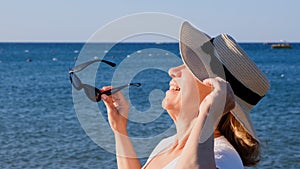happy 50 year old woman in straw hat and sunglasses enjoying the sun against the blue sea background. Summer, vacation