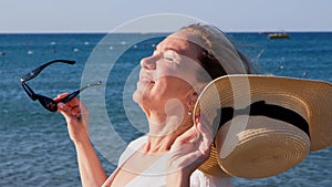 happy 50 year old woman in straw hat and sunglasses enjoying the sun against the blue sea background. Summer, vacation