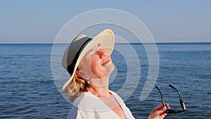 happy 50 year old woman in straw hat and sunglasses enjoying the sun against the blue sea background. Summer, vacation