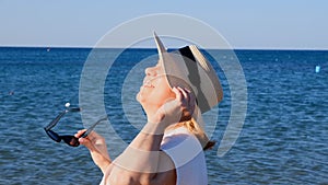 happy 50 year old woman in straw hat and sunglasses enjoying the sun against the blue sea background. Summer, vacation