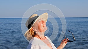 happy 50 year old woman in straw hat and sunglasses enjoying the sun against the blue sea background. Summer, vacation