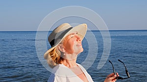 happy 50 year old woman in straw hat and sunglasses enjoying the sun against the blue sea background. Summer, vacation