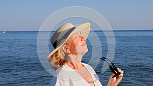 happy 50 year old woman in straw hat and sunglasses enjoying the sun against the blue sea background. Summer, vacation