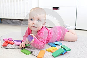 Happy 6 month baby girl plays wooden multicolored meccano