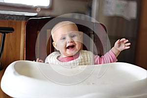 Happy 6 Month Old Baby Girl in Bib Eating at High Chair