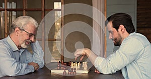 Happy 60s old mature man enjoying playing chess with son.