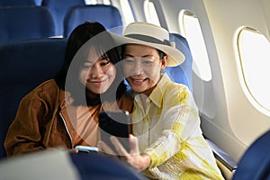 Happy 60s woman and daughter taking photo with smartphone in passenger airplane. Transportation, travel and summer