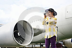 Happy 60s woman in summer clothing taking photo with camera near the airplane.Travel and summer vacation concept