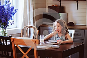 Happy 8 years old child girl having breakfast in country kitchen