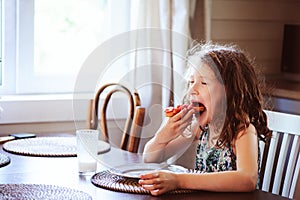 Happy 8 years old child girl having breakfast in country kitchen