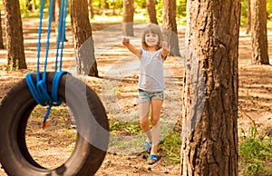 Happy active child girl playing on swing wheel in forest on sunny summer day. Preschool child having fun and swinging on a tire