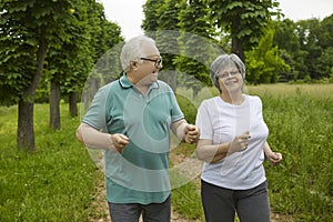 Happy active elderly couple on a summer day jogging outdoors in a park or forest.