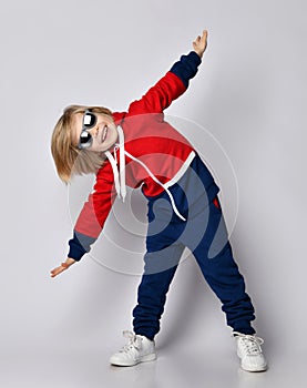 Happy active frolic blond kid boy in blue and red hoodie, pants and sunglasses is playing aircraft pilot