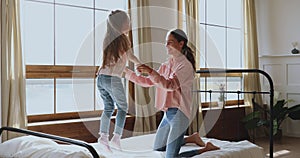 Happy active kid girl jumping on bed playing with mother