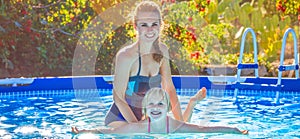 Happy active mother teaching daughter to swim in swimming pool