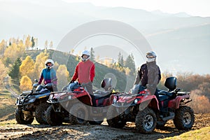 Happy active riders in protective helmets enjoying extreme riding on ATV quad motorbikes in fall mountains at sunset photo