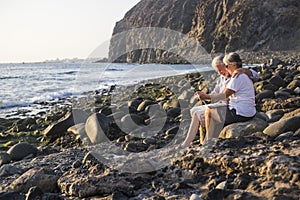 Happy active senior caucasian senior people enjoy the stones beach and work together on a laptop connected computer - modern