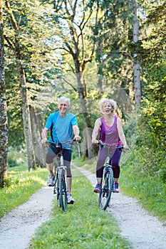 Happy and active senior couple riding bicycles outdoors in the p