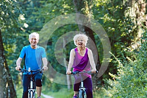 Happy and active senior couple riding bicycles outdoors in the park